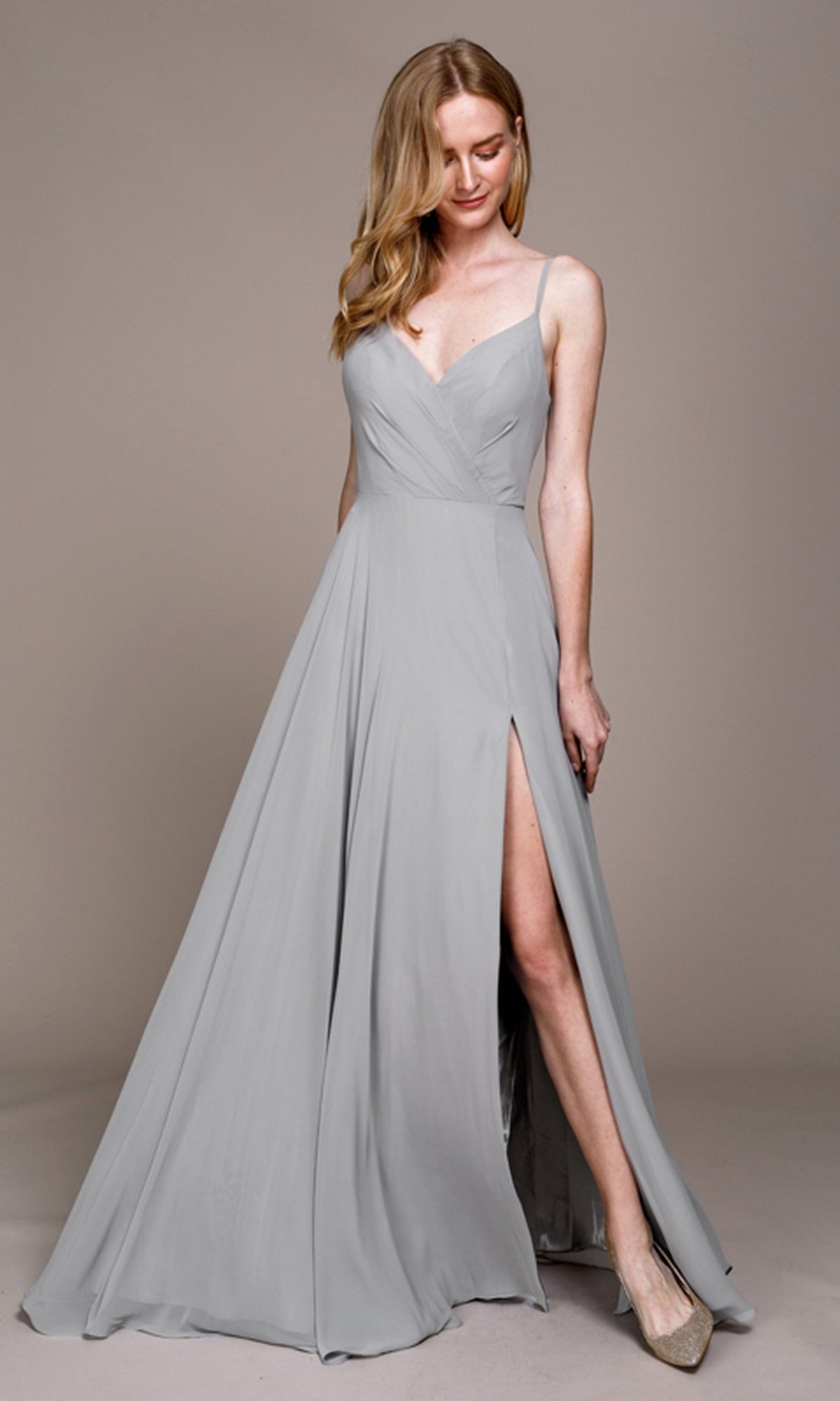 A woman poses in front of a neutral background wearing the Simple V-Neck Long A-Line Prom Dress 477, a light gray sleeveless gown featuring a V-neckline and thigh-high slit.